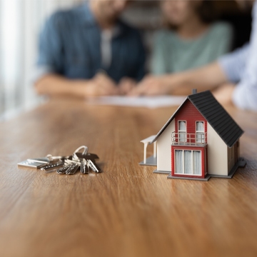 Maison miniature et clés de maison sur la table pendant que les gens parlent en arrière-plan